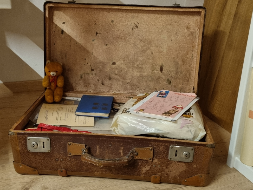 Brauner, geöffneter, alter Koffer mit Teddy und Poesiealbum, der viel für die eigenen Zukunft bedeutet