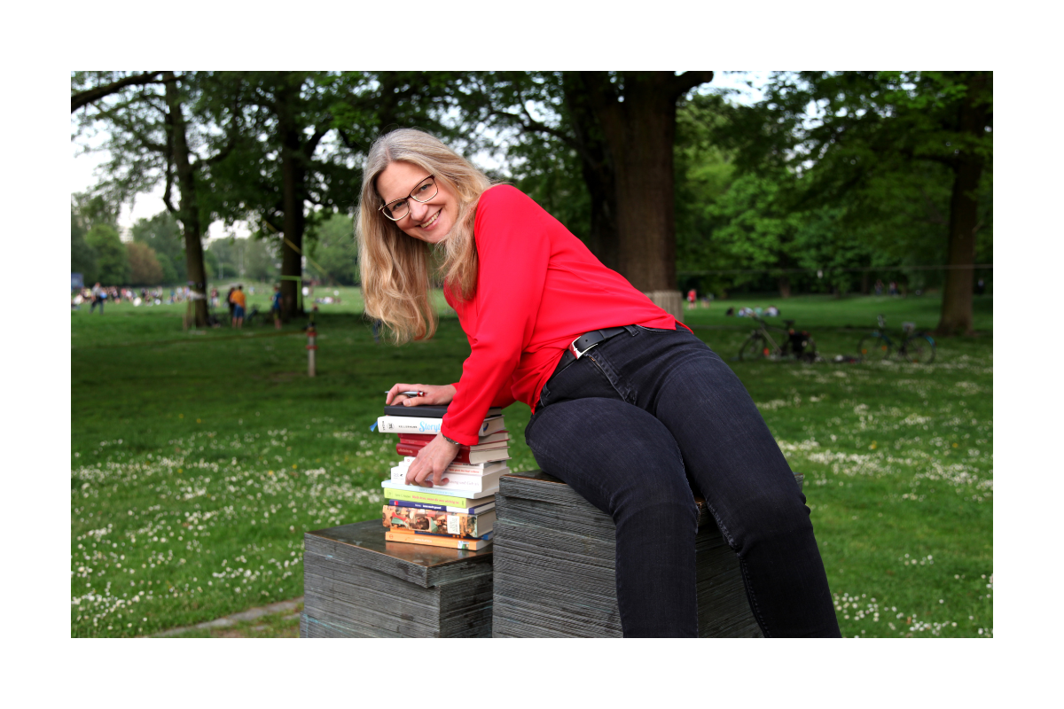 Susanne beugt sich lachend über ihre Bücher im Park