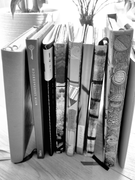 Weibliches Schreiben mit verschiedenen Notiz- und Tagebüchern, die mit ihren dekorativen Buchrücken zu sehen sind.