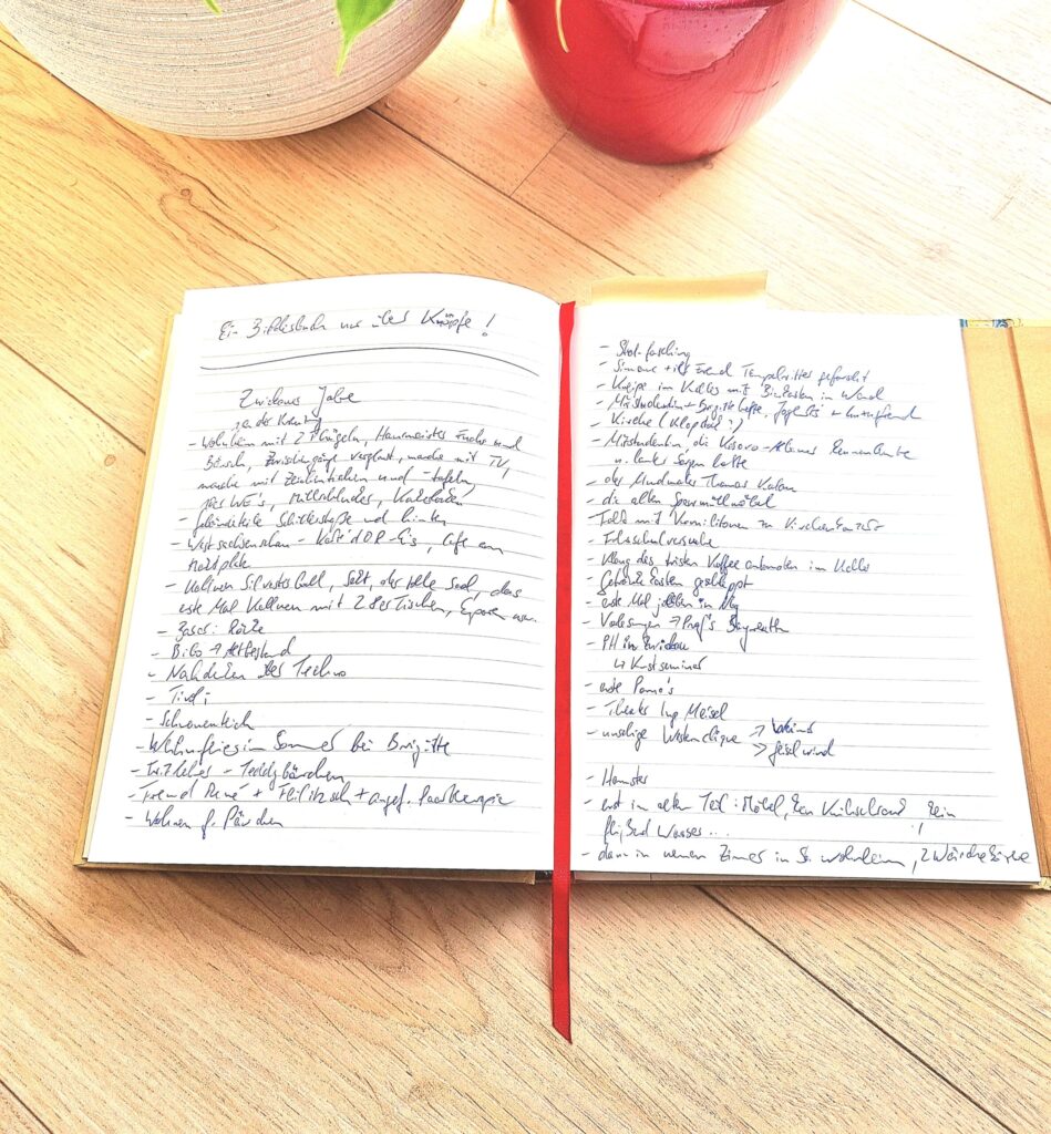Ein aufgeschlagenes Notizbuch mit handschriftlichen Auflistungen vor Blumentöpfen am Boden.