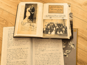 Ein altes Fotoalbum mit Hochzeitspaar liegt aufgeschlagen auf einem Heft mit handgeschriebenem Text